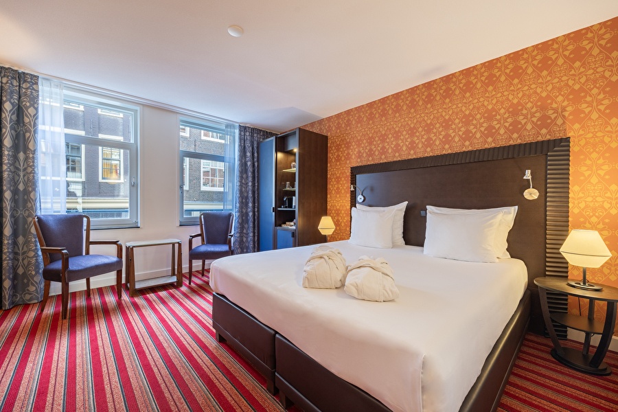Deluxe Room in Grand Hotel Amrâth Amsterdam with double bed, warm colors, sitting area, and view of the historic facades.
