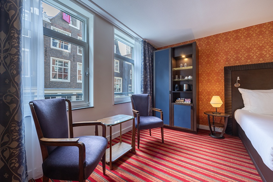 Seating area in a Deluxe room at Grand Hotel Amrâth Amsterdam with views of historical facades and coffee and tea facilities.