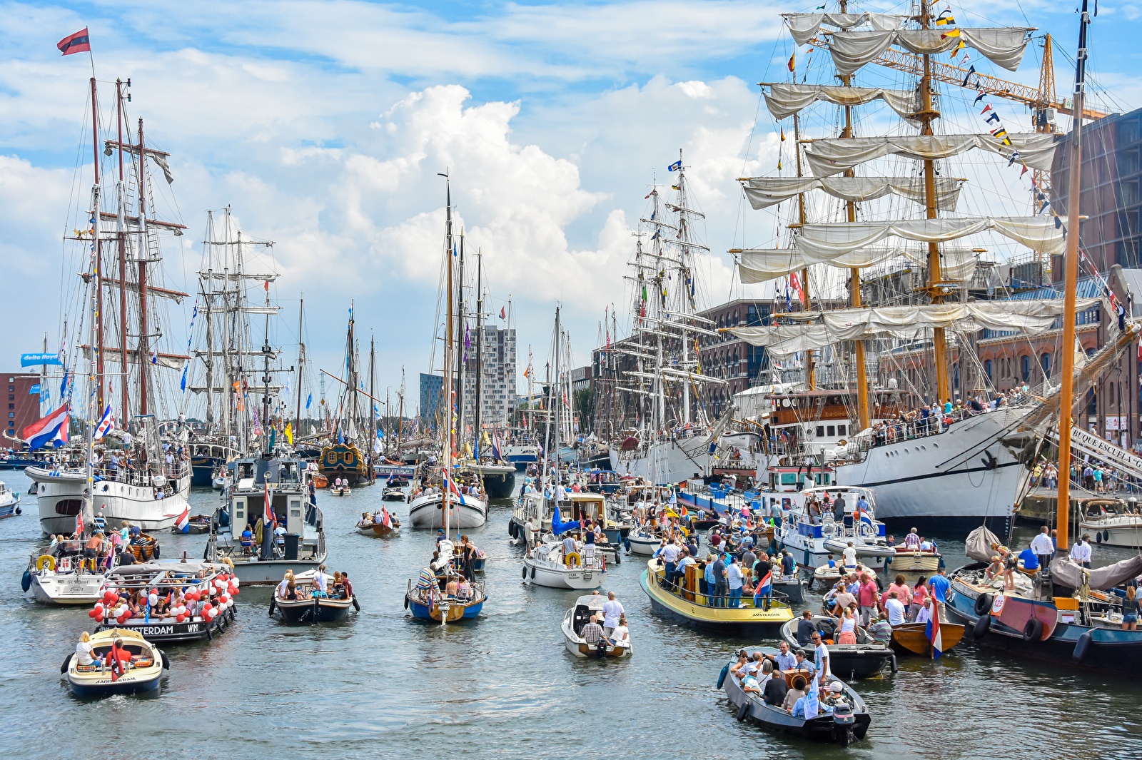 Drukke en feestelijke taferelen tijdens SAIL Amsterdam op het IJ, met tallships, historische schepen en boten vol mensen.