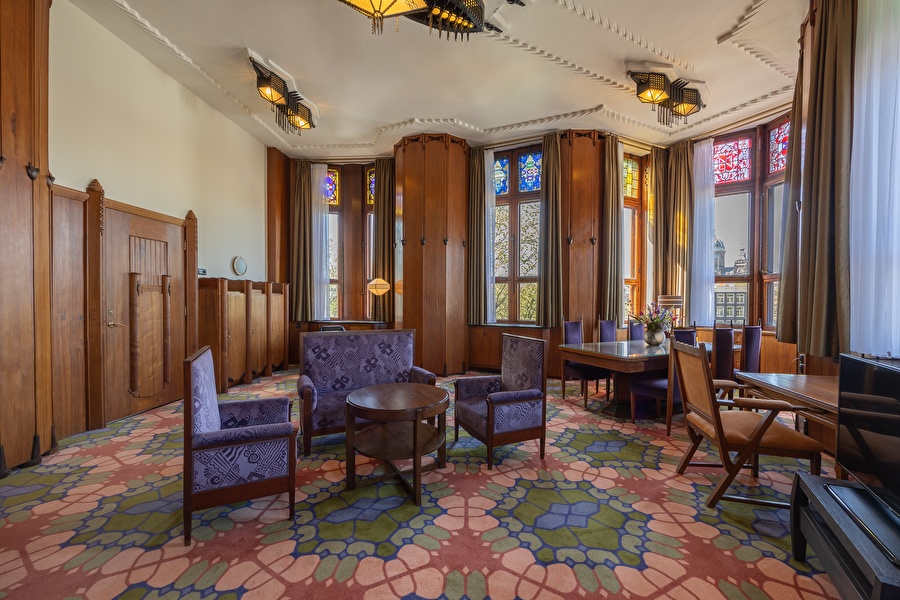 Spacious living room of the Executive Suite with colorful carpet, stained glass windows, and sitting and dining area.