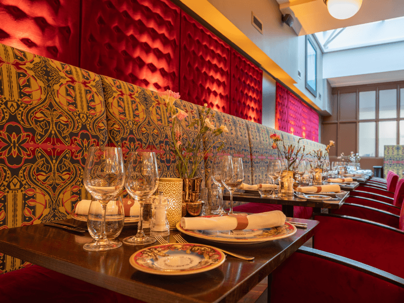 Restaurant Seven Seas in Grand Hotel Amrâth Amsterdam is sfeervol ingericht met rode fluwelen stoelen, en een bank met een print.