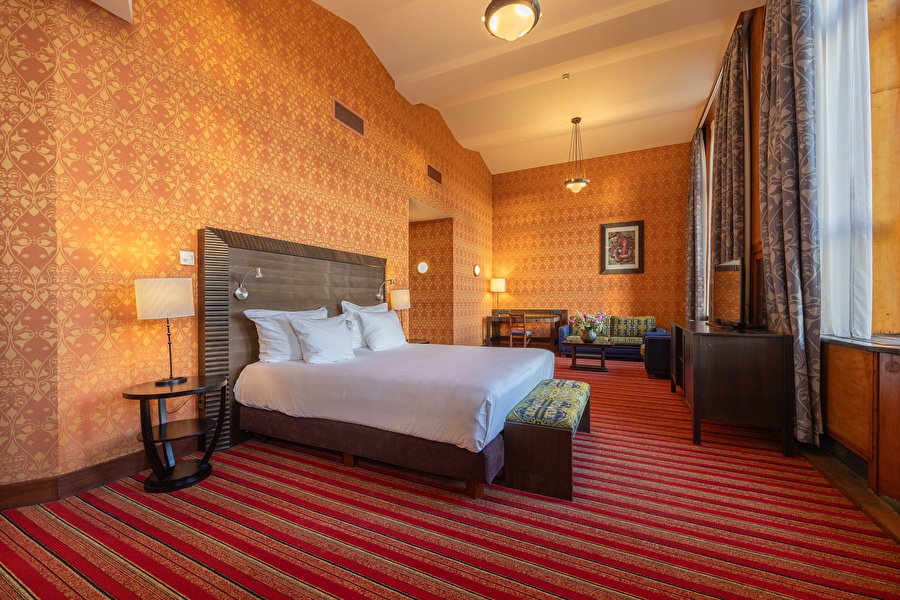 Spacious Junior Suite in Grand Hotel Amrâth Amsterdam with seating area, high windows, and warm art nouveau style.