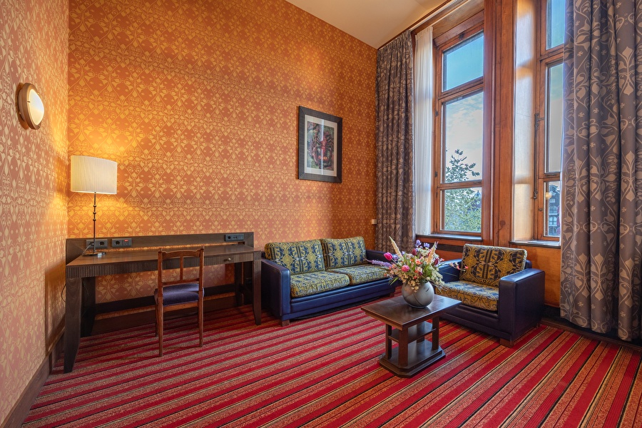 Seating area in the Junior Suite with desk, floral decoration, and city view through tall windows.