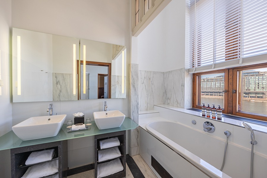 Luxury bathroom of the Junior Suite with double sink, bathtub, and view of the IJ and Amsterdam Central Station.