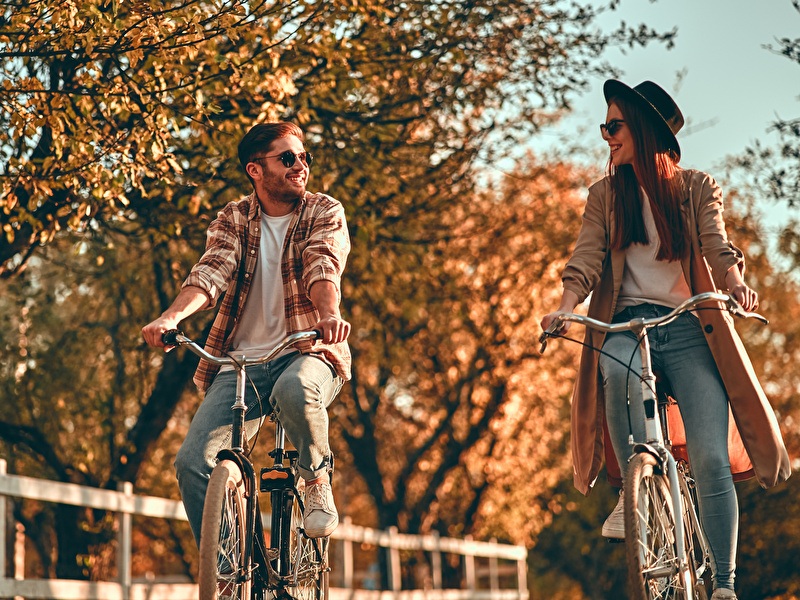 Man en vrouw fietsen lachend naast elkaar op een zonnige herfstdag.
