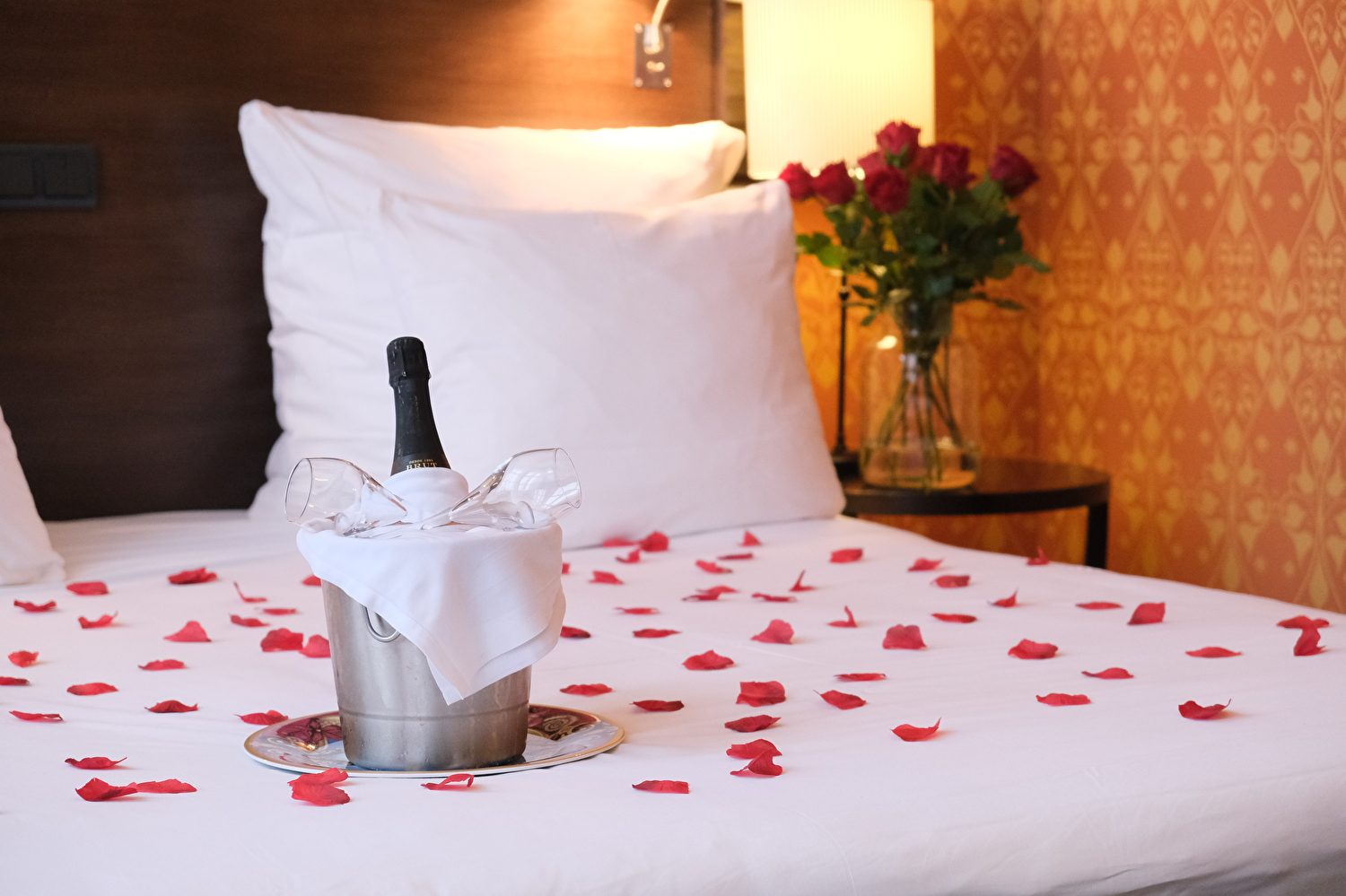 Romantische Szene mit Champagner und Rosenblättern auf dem Bett und Rosen in der Ecke