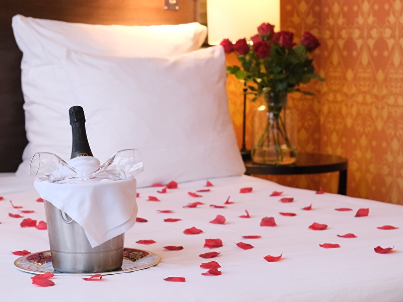 Romantisch tafereel met champagne en rozenblaadjes op bed en rozen in de hoek