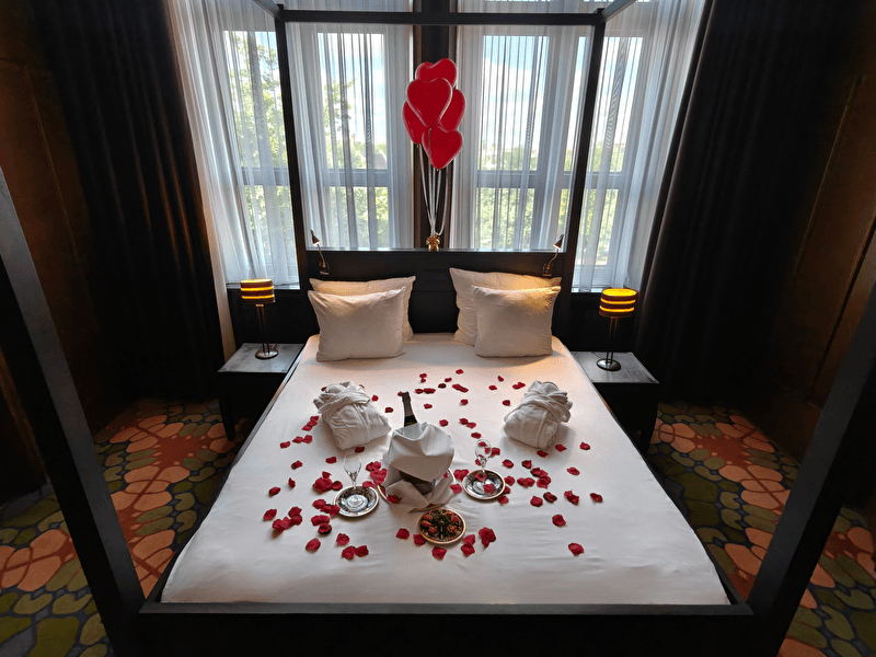 Romantisch tafereel met champagne en rozenblaadjes op bed en rozen in de hoek