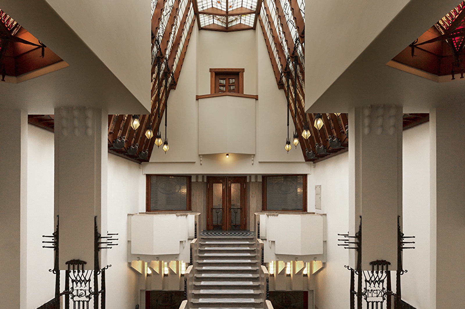 Monumentale trap in het atrium van Grand Hotel Amrâth Amsterdam met glazen dak, art nouveau-details en symmetrische architectuur.