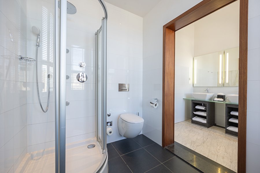 Modern bathroom of the Suite with round shower cabin, separate toilet, and double sink.