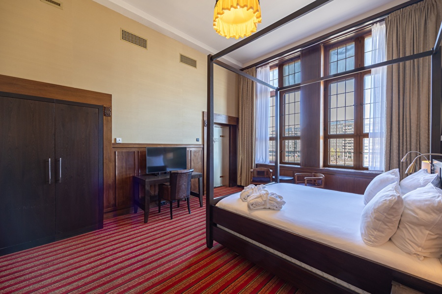 Suite with a canopy bed, red-striped carpet, workspace, and large windows with a view over the Oosterdok.