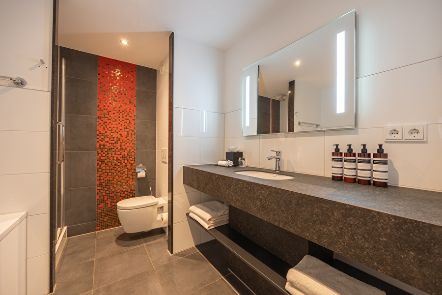 Luxurious bathroom of the Superior Deluxe room with a walk-in shower, red mosaic accent, and double sink.