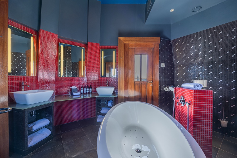 Luxurious bathroom of the Tower Suite with freestanding whirlpool bath, double sink, and red mosaic tiles.