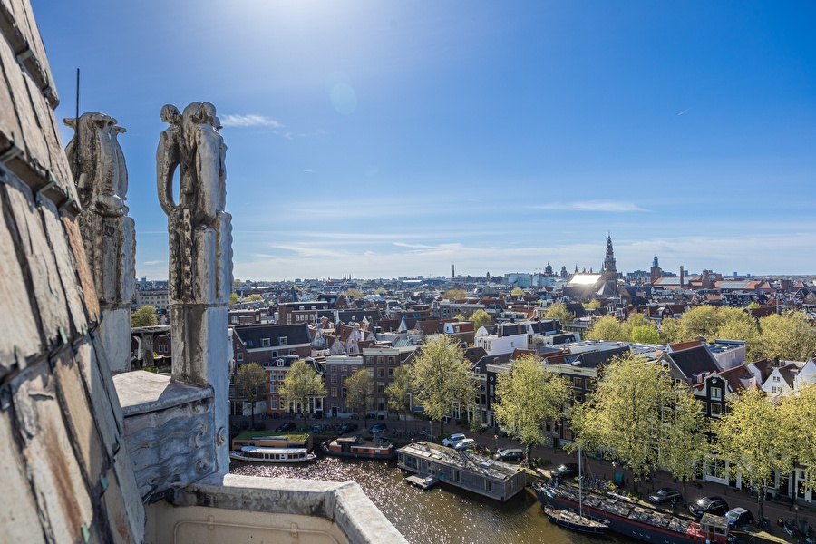 View from the Tower Suite over the rooftops, canals, and towers of Amsterdam, flanked by art-nouveau sculptures.