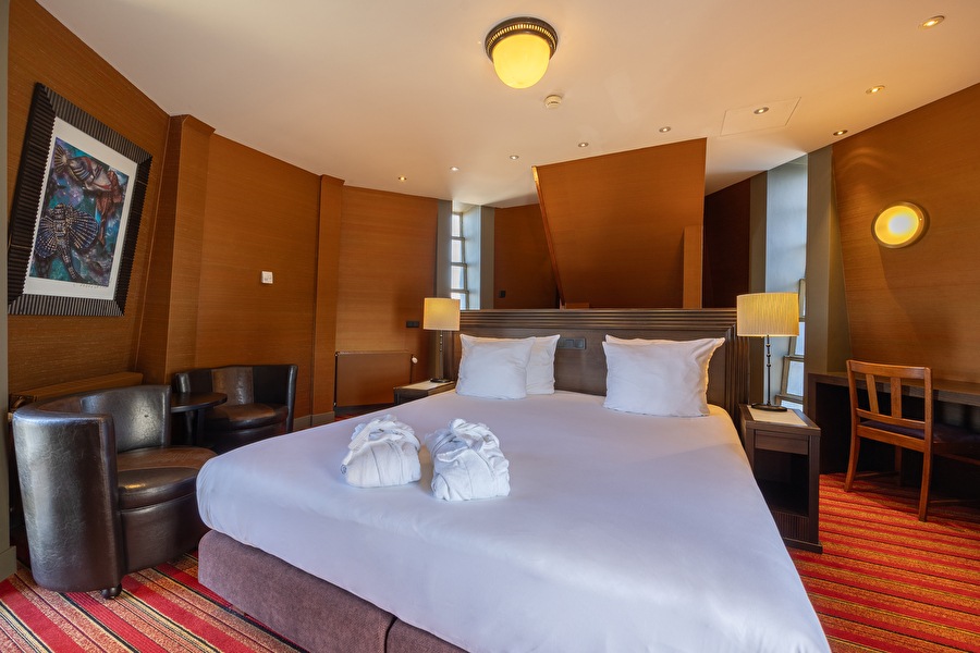Luxurious bedroom of the Tower Suite with king-sized bed, warm wooden accents, and red striped carpet.